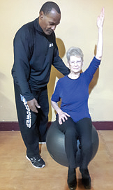Mark Bryant with Dorene Cropley. “This exercise helps with muscle stability and balance, it improves coordination and posture. Dorene is sitting on the Fit-Ball, lifting her left arm at the same time she lifts her right knee. It’s harder than it looks!” says Mark. 