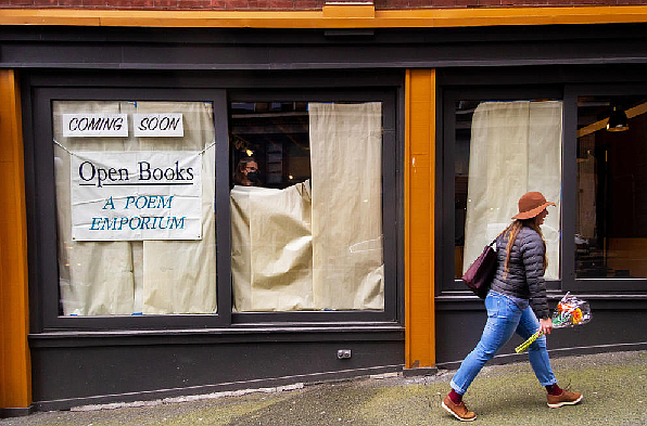 A customer walks in front of the new Pioneer Square location of Open Books, a longtime Seattle poetry-only bookstore reopening this month, while owner Billie Swift takes down the paper covering the windows. (Margo Vansynghel/Crosscut)