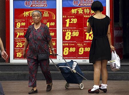 Shoppers walk past and look at a board displaying food prices at a shopping mall in central Beijing August 9, 2011. REUTERS/David Gray